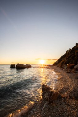 Gün doğumunda gizli körfez. Küçük kuma, çakıl taşına, sıcak renklerde plaja ve sabah ışığına baktım. Xigia Sülfür Plajları 'ndaki deniz manzarası, İyon Adaları, Yunanistan