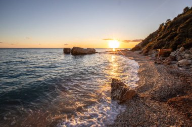 Gün doğumunda gizli körfez. Küçük kuma, çakıl taşına, sıcak renklerde plaja ve sabah ışığına baktım. Xigia Sülfür Plajları 'ndaki deniz manzarası, İyon Adaları, Yunanistan