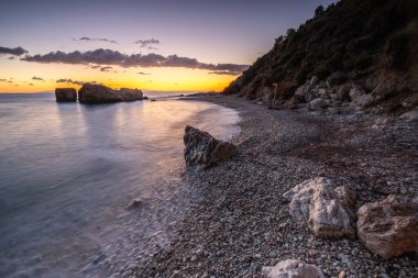 Gün doğumunda gizli körfez. Küçük kuma, çakıl taşına, sıcak renklerde plaja ve sabah ışığına baktım. Xigia Sülfür Plajları 'ndaki deniz manzarası, İyon Adaları, Yunanistan