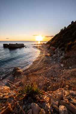 Gün doğumunda gizli körfez. Küçük kuma, çakıl taşına, sıcak renklerde plaja ve sabah ışığına baktım. Xigia Sülfür Plajları 'ndaki deniz manzarası, İyon Adaları, Yunanistan