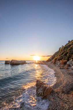 Gün doğumunda gizli körfez. Küçük kuma, çakıl taşına, sıcak renklerde plaja ve sabah ışığına baktım. Xigia Sülfür Plajları 'ndaki deniz manzarası, İyon Adaları, Yunanistan