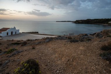 Yunanistan 'ın tipik mimari tarzında küçük beyaz bir kilise. Akdeniz ve güneşin doğuşuyla çevrili bir ağacın üzerinde duruyor. Agios Nikolaos Şapeli, İyon Adaları, Yunanistan