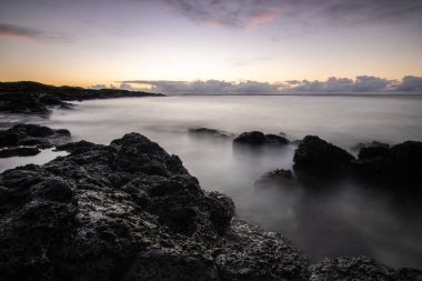 Denizin üzerinde uzun süre güneş doğuyor. Lav taşlı kum kumsalı ve mavi suyla alternatif mavi su. Hint Okyanusu 'nda bir ada, beklenmedik bir plaj, Trou dEau Douce, Mauritius, Afrika