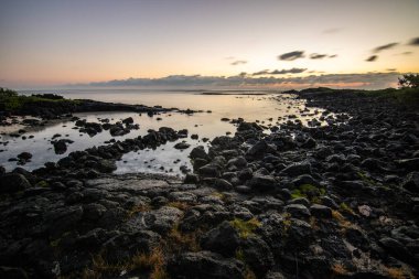 Küçük dalgalar lav kayalarını denizle çevreler. Hint Okyanusu 'ndaki bir adanın kıyı şeridi. Sabah gün doğumu, sahilde güzel sıcak bir ışık... Trou d 'Eau Douce, Mauritius