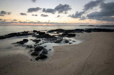 Küçük dalgalar lav kayalarını denizle çevreler. Hint Okyanusu 'ndaki bir adanın kıyı şeridi. Sabah gün doğumu, sahilde güzel sıcak bir ışık... Trou d 'Eau Douce, Mauritius