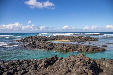 Küçük dalgalar lav kayalarını denizle çevreler. Hint Okyanusu 'ndaki bir adanın kıyı şeridi. Sabah gün doğumu, sahilde güzel sıcak bir ışık... Trou d 'Eau Douce, Mauritius