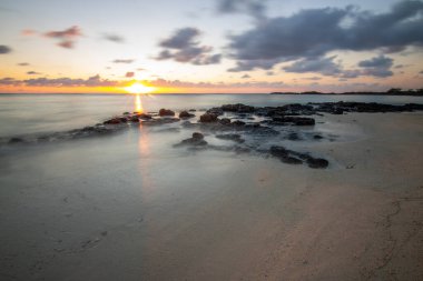 Küçük dalgalar lav kayalarını denizle çevreler. Hint Okyanusu 'ndaki bir adanın kıyı şeridi. Sabah gün doğumu, sahilde güzel sıcak bir ışık... Trou d 'Eau Douce, Mauritius