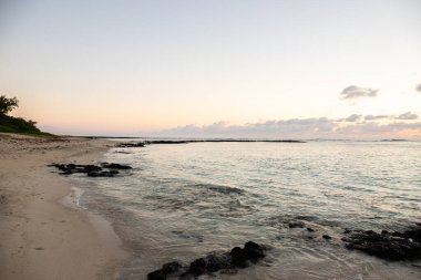Küçük dalgalar lav kayalarını denizle çevreler. Hint Okyanusu 'ndaki bir adanın kıyı şeridi. Sabah gün doğumu, sahilde güzel sıcak bir ışık... Trou d 'Eau Douce, Mauritius