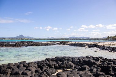 Küçük dalgalar lav kayalarını denizle çevreler. Hint Okyanusu 'ndaki bir adanın kıyı şeridi. Sabah gün doğumu, sahilde güzel sıcak bir ışık... Trou d 'Eau Douce, Mauritius