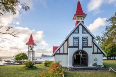 Kırmızı çatılı küçük bir kilise manzaralı manzara. Körfez ve balıkçı tekneleri olan küçük liman. Günbatımı manzaralı tropik manzara, Notre-Dame Auxiliatrice de Cap Malheureux, Mauritius