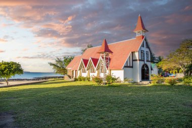 Landscape with a view of a small church with a red roof. Bay and small harbor with fishing boats. Tropical landscape with sunset view, Notre-Dame Auxiliatrice de Cap Malheureux, Mauritius clipart