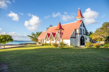Kırmızı çatılı küçük bir kilise manzaralı manzara. Körfez ve balıkçı tekneleri olan küçük liman. Günbatımı manzaralı tropik manzara, Notre-Dame Auxiliatrice de Cap Malheureux, Mauritius
