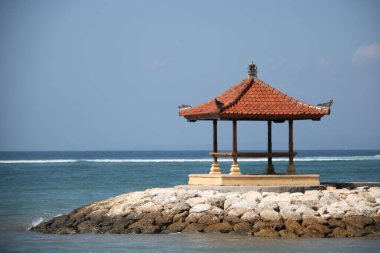 Sahilde muhteşem bir gün doğumu. Küçük tapınakları var. Dalgakıran olarak inşa edilmiş. Ufukta deniz manzarası var. Sanur, Bali, Endonezya