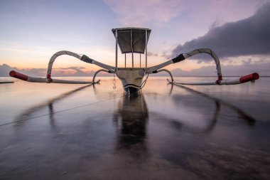 Sahilde küçük tapınaklar ve geleneksel balıkçı teknesi Jukung 'la muhteşem bir gün doğumu. Ufukta deniz manzarası var. Sanur, Bali, Endonezya