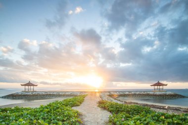Sahilde muhteşem bir gün doğumu. Küçük tapınakları var. Dalgakıran olarak inşa edilmiş. Ufukta deniz manzarası var. Sanur, Bali, Endonezya