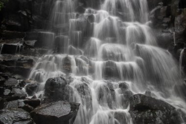 Güzel gizli şelale bir çok kattan aşağı düşüyor. Siyah lav taşlarıyla çevrili Kanto Lampo, Bali, Endonezya