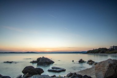 Kumlu bir sahildeki kayaların arasından gün batımına bak. Manzara, Ouranoupoli, Selanik, Orta Makedonya ve Yunanistan kıyılarındaki engin deniz manzarası ile çekildi