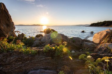 Kumlu bir sahildeki kayaların arasından gün batımına bak. Manzara, Ouranoupoli, Selanik, Orta Makedonya ve Yunanistan kıyılarındaki engin deniz manzarası ile çekildi