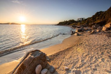 Kumlu bir sahildeki kayaların arasından gün batımına bak. Manzara, Ouranoupoli, Selanik, Orta Makedonya ve Yunanistan kıyılarındaki engin deniz manzarası ile çekildi