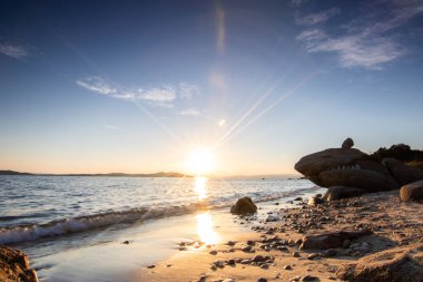 Kumlu bir sahildeki kayaların arasından gün batımına bak. Manzara, Ouranoupoli, Selanik, Orta Makedonya ve Yunanistan kıyılarındaki engin deniz manzarası ile çekildi