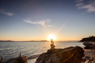 Kumlu bir sahildeki kayaların arasından gün batımına bak. Manzara, Ouranoupoli, Selanik, Orta Makedonya ve Yunanistan kıyılarındaki engin deniz manzarası ile çekildi