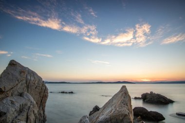 Kumlu bir sahildeki kayaların arasından gün batımına bak. Manzara, Ouranoupoli, Selanik, Orta Makedonya ve Yunanistan kıyılarındaki engin deniz manzarası ile çekildi