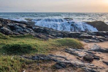 Akşama kumsalda, gün batımında. Vahşi dalgalı taşlı kıyı kesimi. Denizin üzerinde gün batımını gösteren manzara. Bentota, Sri Lanka, Asya yakınlarındaki ufuk manzarası