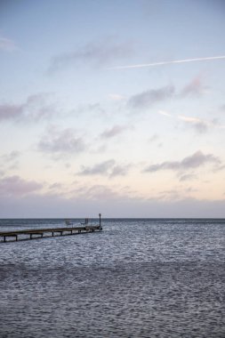 Sunrise over a lake in autumn. A wooden jetty protrudes into the water while grass has established itself on the sandy beach. The lake and beach, located on Lake Vnern in Ns Sannar, Sweden, Scandina clipart