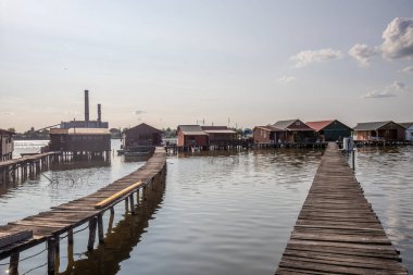 Sudaki ahşap evler. Gün batımında gölde tatil beldesi. Uzun ahşap yollar bireysel evlere çıkıyor. Macaristan, Balaton Gölü, Bokodi 'nin yüzen köyünün manzara fotoğrafı.