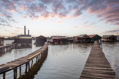 Wooden houses in the water. Holiday resort in the lake at sunset. Long wooden walkways lead to the individual houses. Landscape photo of the floating village of Bokodi, Lake Balaton, Hungary clipart