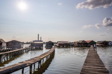 Sudaki ahşap evler. Gün batımında gölde tatil beldesi. Uzun ahşap yollar bireysel evlere çıkıyor. Macaristan, Balaton Gölü, Bokodi 'nin yüzen köyünün manzara fotoğrafı.