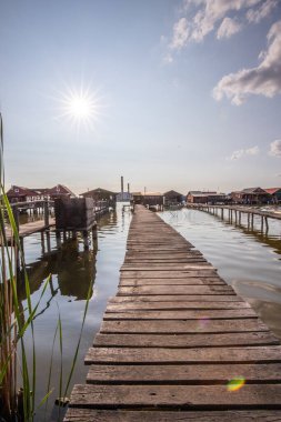 Wooden houses in the water. Holiday resort in the lake at sunset. Long wooden walkways lead to the individual houses. Landscape photo of the floating village of Bokodi, Lake Balaton, Hungary clipart