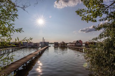 Sudaki ahşap evler. Gün batımında gölde tatil beldesi. Uzun ahşap yollar bireysel evlere çıkıyor. Macaristan, Balaton Gölü, Bokodi 'nin yüzen köyünün manzara fotoğrafı.