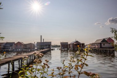 Sudaki ahşap evler. Gün batımında gölde tatil beldesi. Uzun ahşap yollar bireysel evlere çıkıyor. Macaristan, Balaton Gölü, Bokodi 'nin yüzen köyünün manzara fotoğrafı.