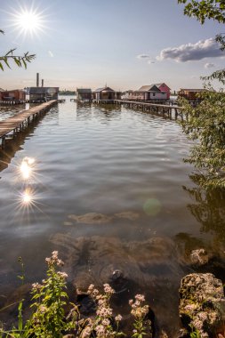 Sudaki ahşap evler. Gün batımında gölde tatil beldesi. Uzun ahşap yollar bireysel evlere çıkıyor. Macaristan, Balaton Gölü, Bokodi 'nin yüzen köyünün manzara fotoğrafı.