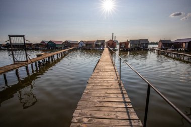 Wooden houses in the water. Holiday resort in the lake at sunset. Long wooden walkways lead to the individual houses. Landscape photo of the floating village of Bokodi, Lake Balaton, Hungary clipart