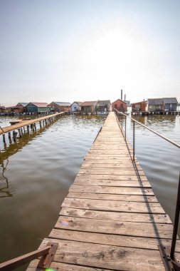 Sudaki ahşap evler. Gün batımında gölde tatil beldesi. Uzun ahşap yollar bireysel evlere çıkıyor. Macaristan, Balaton Gölü, Bokodi 'nin yüzen köyünün manzara fotoğrafı.