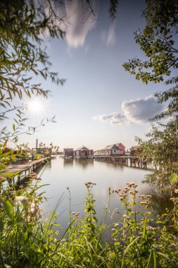 Sudaki ahşap evler. Gün batımında gölde tatil beldesi. Uzun ahşap yollar bireysel evlere çıkıyor. Macaristan, Balaton Gölü, Bokodi 'nin yüzen köyünün manzara fotoğrafı.