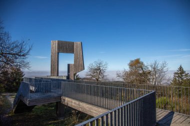 Wooden sculpture with a steel walkway and viewpoint. Landscape shot on a mountain, blue sky fog in the valley. Morning at the Erbeskopf wind sound sculpture, Hilscheid, Rhineland-Palatinate, Germany clipart