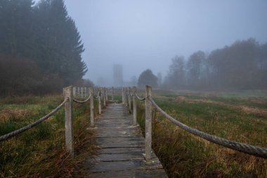 A wooden walkway or pier leads through a nature reserve in thick fog. Landscape shot in the middle of nature in autumn. Baldenau castle ruins, Morbach, Hunsrck, Rhineland Palatinate clipart