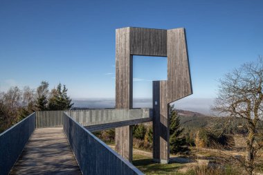 Wooden sculpture with a steel walkway and viewpoint. Landscape shot on a mountain, blue sky fog in the valley. Morning at the Erbeskopf wind sound sculpture, Hilscheid, Rhineland-Palatinate, Germany clipart