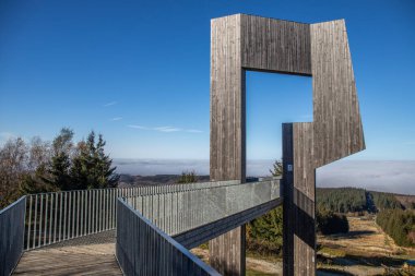 Çelik yolu ve bakış açısı olan ahşap heykel. Dağ manzarası, vadide mavi gökyüzü sisi. Erbeskopf rüzgar ses heykelinde sabah, Hilscheid, Rhineland-Palatinate, Almanya