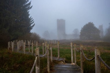 A wooden walkway or pier leads through a nature reserve in thick fog. Landscape shot in the middle of nature in autumn. Baldenau castle ruins, Morbach, Hunsrck, Rhineland Palatinate clipart