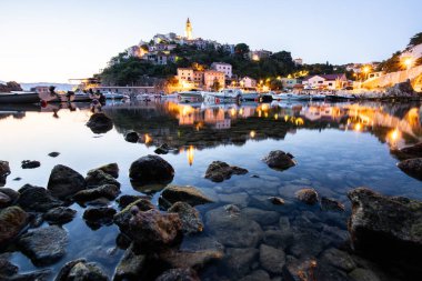 Liman ve sahil, tepenin üstünde eski bir köy. Gemiler suya yansıyor, güneş Adriyatik 'in ufuklarından doğuyor. Vrbnik, Krk, Hırvatistan 'dan güzel manzara görüntüleri