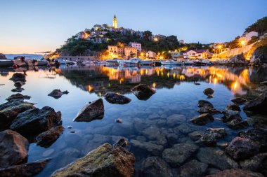 Liman ve sahil, tepenin üstünde eski bir köy. Gemiler suya yansıyor, güneş Adriyatik 'in ufuklarından doğuyor. Vrbnik, Krk, Hırvatistan 'dan güzel manzara görüntüleri