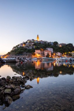 Liman ve sahil, tepenin üstünde eski bir köy. Gemiler suya yansıyor, güneş Adriyatik 'in ufuklarından doğuyor. Vrbnik, Krk, Hırvatistan 'dan güzel manzara görüntüleri
