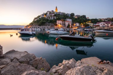 Liman ve sahil, tepenin üstünde eski bir köy. Gemiler suya yansıyor, güneş Adriyatik 'in ufuklarından doğuyor. Vrbnik, Krk, Hırvatistan 'dan güzel manzara görüntüleri