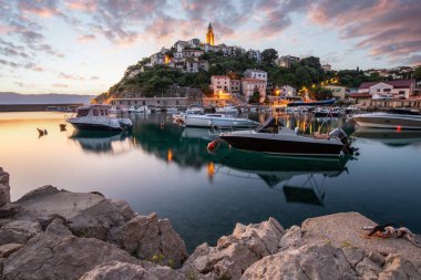 Liman ve sahil, tepenin üstünde eski bir köy. Gemiler suya yansıyor, güneş Adriyatik 'in ufuklarından doğuyor. Vrbnik, Krk, Hırvatistan 'dan güzel manzara görüntüleri