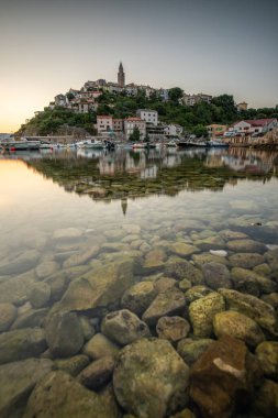 Liman ve sahil, tepenin üstünde eski bir köy. Gemiler suya yansıyor, güneş Adriyatik 'in ufuklarından doğuyor. Vrbnik, Krk, Hırvatistan 'dan güzel manzara görüntüleri