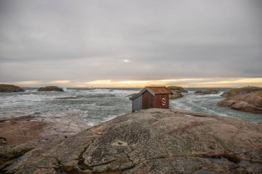 Gün batımında güzel bir sahil fotoğrafı. Dik bir sahil manzarası doğa koruma alanında. İsveç için tipik binalar kırmızı evde bulunabilir. Grebbestad, İsveç, İskandinavya